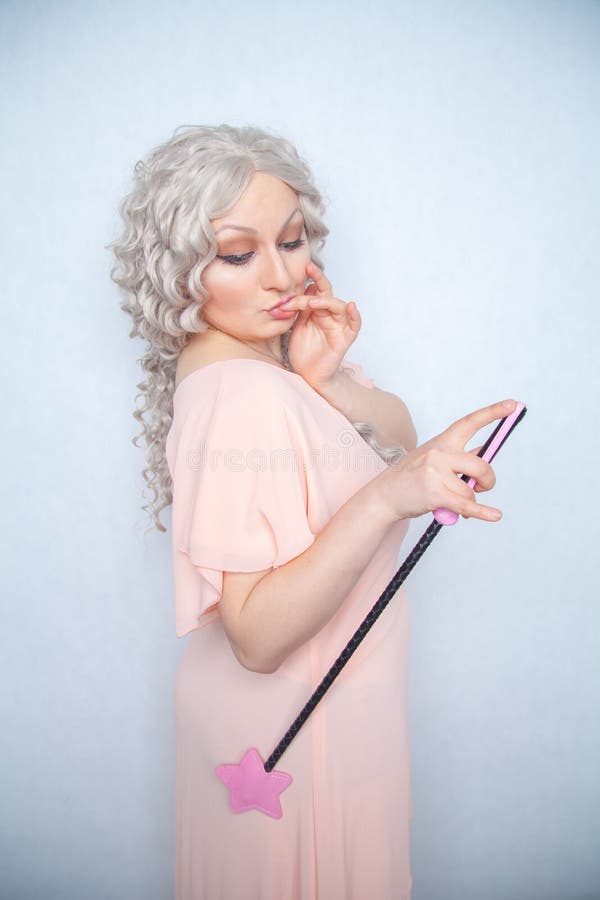 Donna graziosa crespa con il raccolto di guida rosa della stella la donna bionda sveglia tiene la frusta del bdsm sul fondo solid fotografie stock Donna graziosa crespa con il raccolto di guida rosa della stella la donna bionda sveglia tiene la frusta del bdsm sul fondo solid fotografie stock