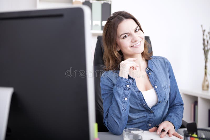 Donna graziosa dell'ufficio che sorride al suo Worktable fotografia stock libera da diritti Donna graziosa dell'ufficio che sorride al suo Worktable fotografia stock libera da diritti