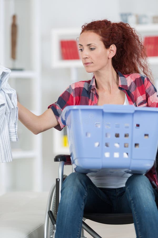 Donna handicappata che si siede in sedia a rotelle che fa lavanderia a casa immagini stock Donna handicappata che si siede in sedia a rotelle che fa lavanderia a casa immagini stock