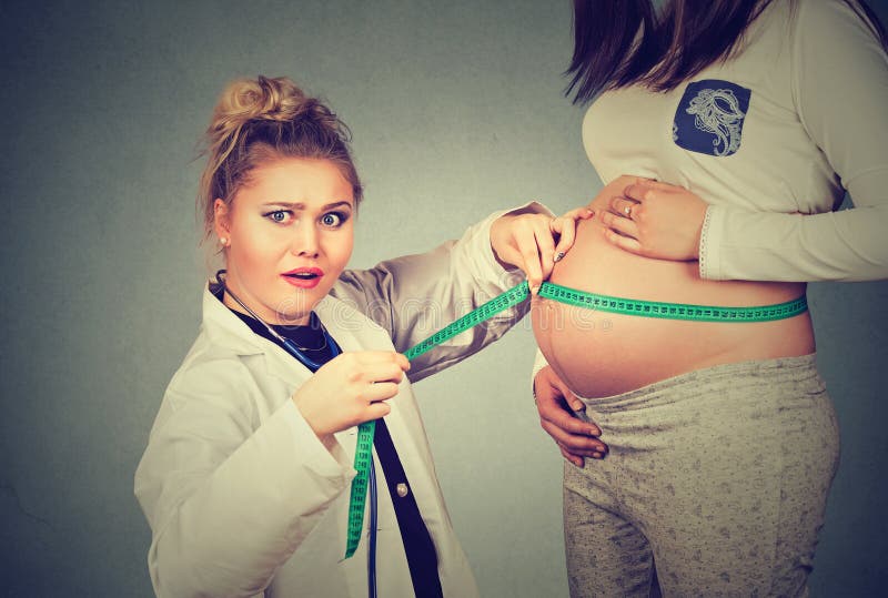 Donna incinta che espone pancia mentre un medico colpito del ginecologo utilizza il nastro di misurazione per seguire la crescita fotografia stock libera da diritti Donna incinta che espone pancia mentre un medico colpito del ginecologo utilizza il nastro di misurazione per seguire la crescita fotografia stock libera da diritti