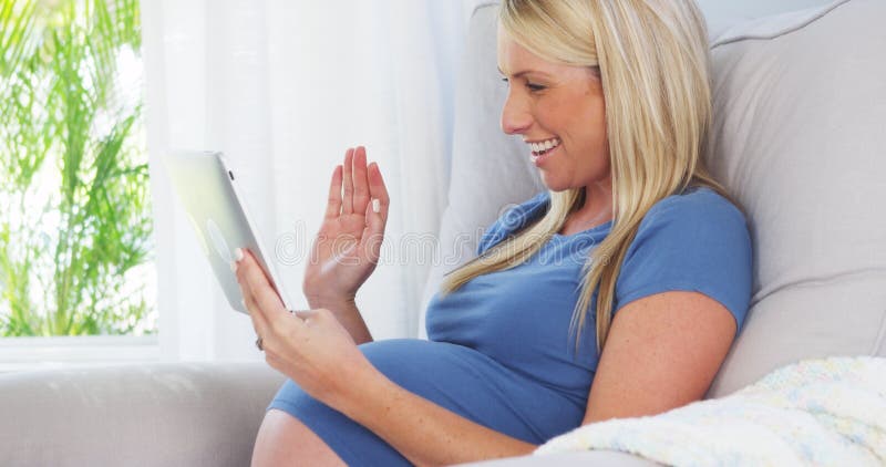 Donna incinta felice che per mezzo della compressa immagine stock libera da diritti Donna incinta felice che per mezzo della compressa immagine stock libera da diritti