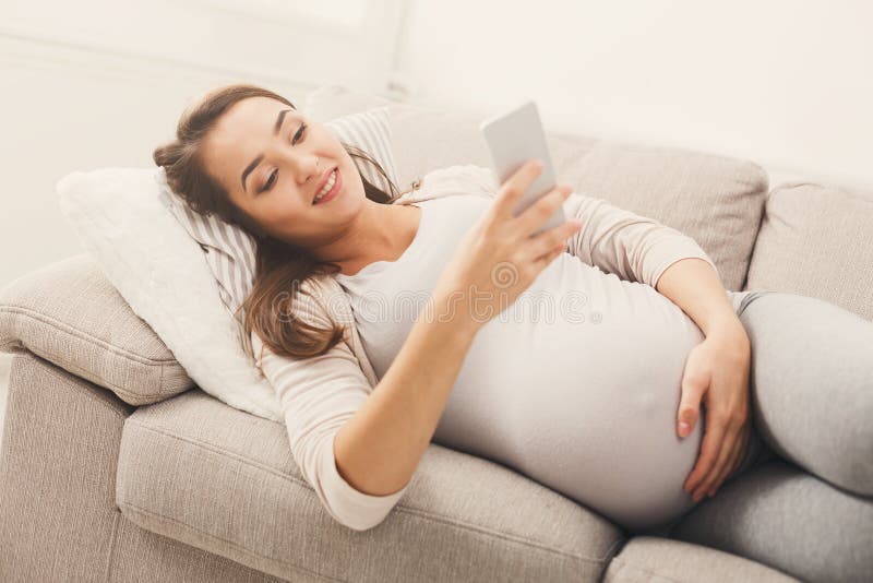 Donna incinta felice che per mezzo dello smartphone fotografia stock Donna incinta felice che per mezzo dello smartphone fotografia stock