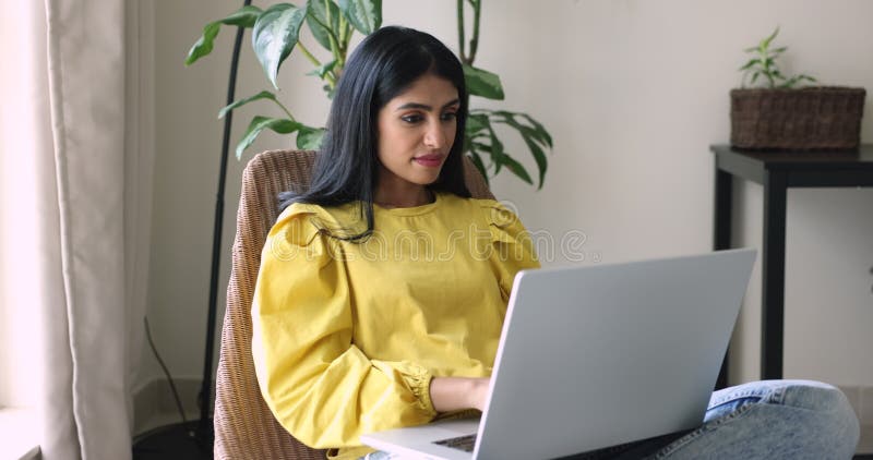 Donna indiana positiva che scrive sul computer portatile poggiando su una comoda poltrona stock footage