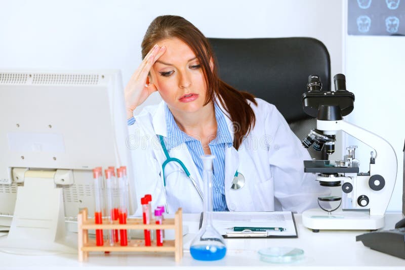 Donna interessata del medico che si siede alla tabella dell'ufficio fotografia stock libera da diritti Donna interessata del medico che si siede alla tabella dell'ufficio fotografia stock libera da diritti