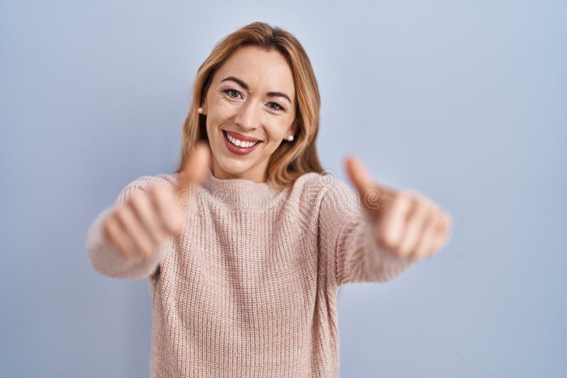 Donna ispanica in piedi su sfondo blu che approva un gesto positivo con i pollici delle mani sorridente e felice per il successo fotografia stock libera da diritti