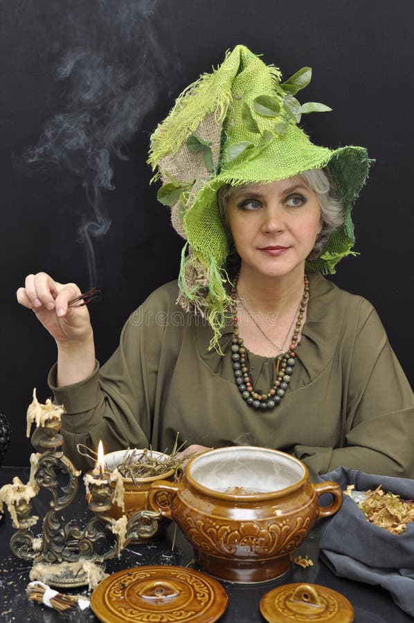 Donna magica in cappello verde con i ramoscelli di fumo fotografia stock Donna magica in cappello verde con i ramoscelli di fumo fotografia stock