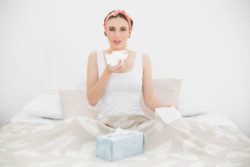 Donna malata che tiene un fazzoletto che si siede sul suo letto fotografie stock libere da diritti Donna malata che tiene un fazzoletto che si siede sul suo letto fotografie stock libere da diritti