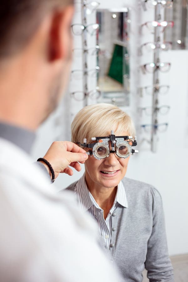 Donna matura sorridente che ha l'esame di vista e misura della diottria da un optometrista maschio fotografia stock