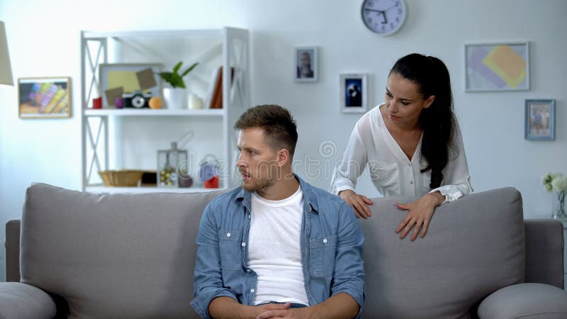Donna nervosa che critica il marito pigro seduto sul divano, conflitto di famiglia, problema