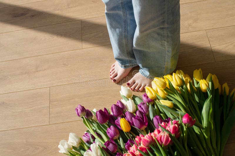 Donna a piedi nudi in piedi accanto a una colorata serie di tulipani su un pavimento di legno fotografia stock