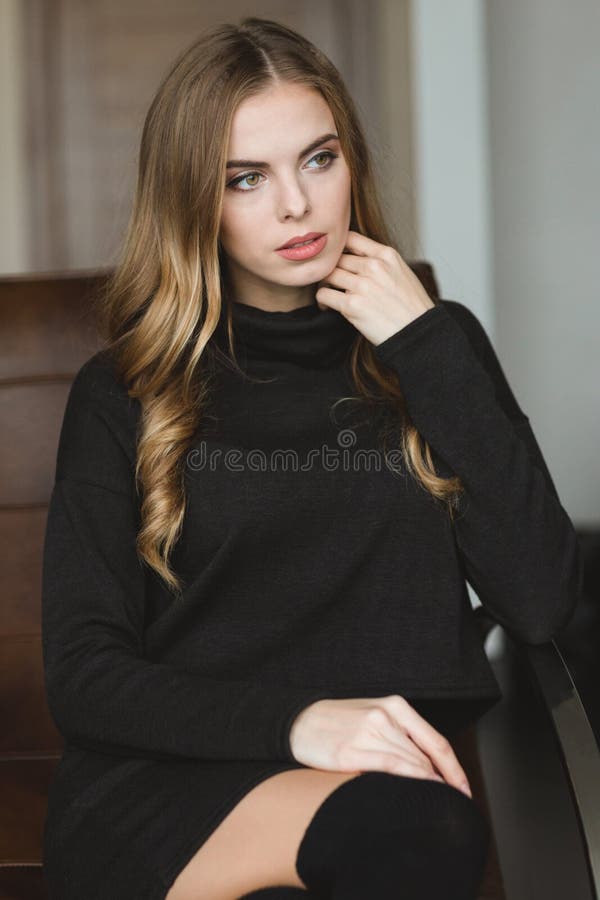 Donna premurosa splendida in vestito nero che si siede sul sofà di cuoio fotografie stock Donna premurosa splendida in vestito nero che si siede sul sofà di cuoio fotografie stock