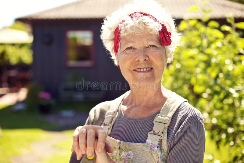 Donna senior attiva che sta nel giardino del cortile fotografia stock Donna senior attiva che sta nel giardino del cortile fotografia stock