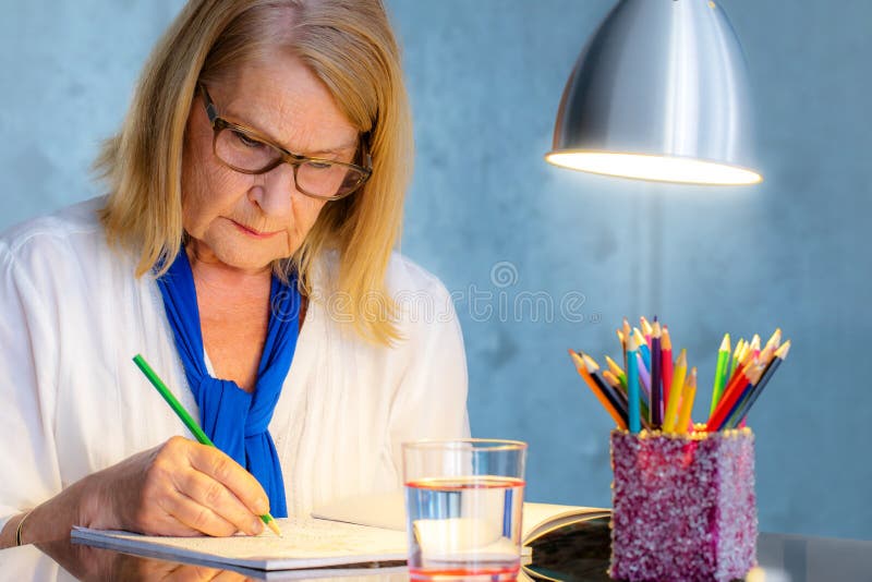 Donna senior che assorbe il libro di colore per gli adulti fotografia stock Donna senior che assorbe il libro di colore per gli adulti fotografia stock