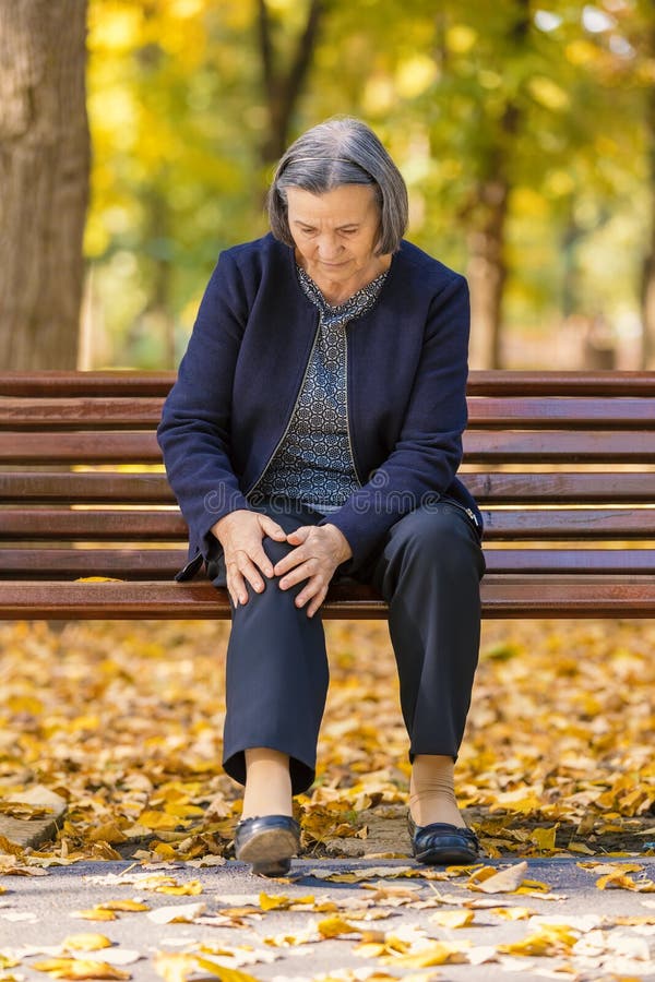 Donna senior che ha dolore del ginocchio che si siede sul banco in parco