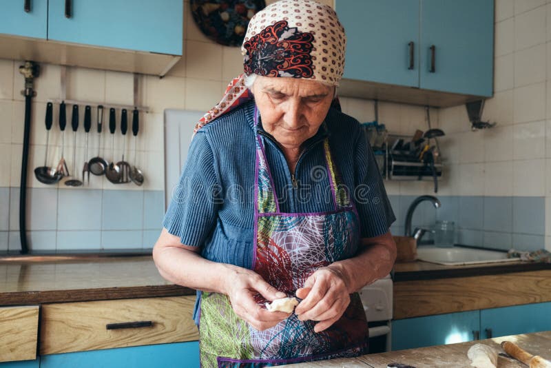Donna senior che impasta la pasta nella sua cucina domestica immagini stock Donna senior che impasta la pasta nella sua cucina domestica immagini stock