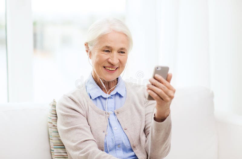 Donna anziana con smartphone e cuffie a casa immagine stock