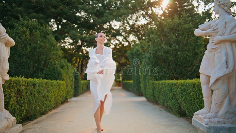 Donna serena che cammina per il bel giardino verde con la sciarpa che nuota nel vento.