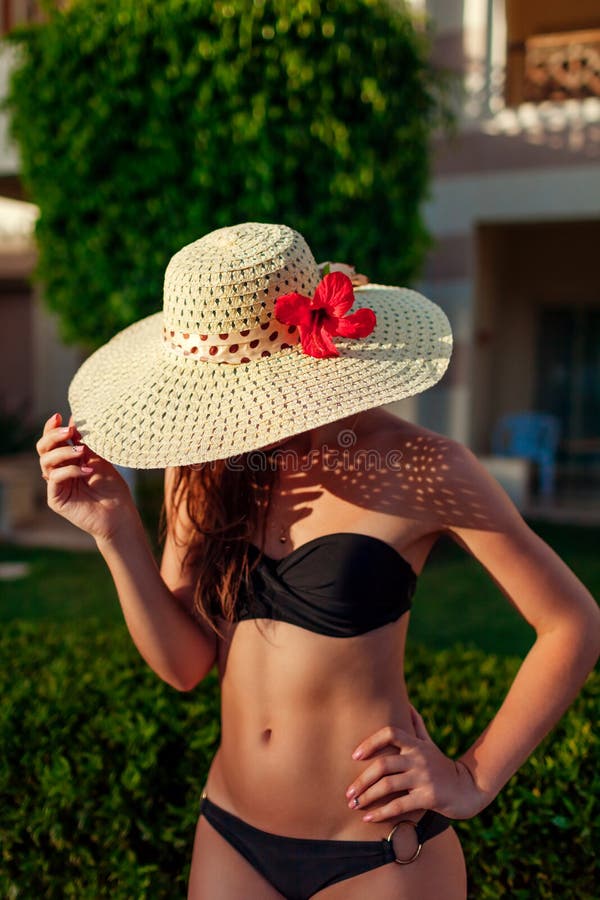 Donna sexy nel fronte nascondentesi del bikini nero con il cappello nel giardino dell'hotel Vacanze estive sulla localit? di sogg fotografia stock Donna sexy nel fronte nascondentesi del bikini nero con il cappello nel giardino dell'hotel Vacanze estive sulla localit? di sogg fotografia stock