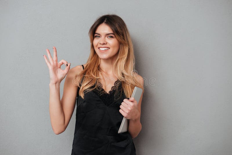 Donna sicura sorridente che mostra gesto giusto e tenuta del computer della compressa fotografie stock libere da diritti Donna sicura sorridente che mostra gesto giusto e tenuta del computer della compressa fotografie stock libere da diritti