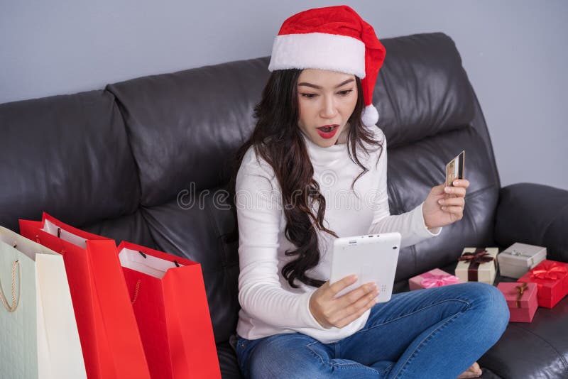 Donna sorpresa in cappello di Santa che compera online per il regalo di Natale fotografia stock Donna sorpresa in cappello di Santa che compera online per il regalo di Natale fotografia stock