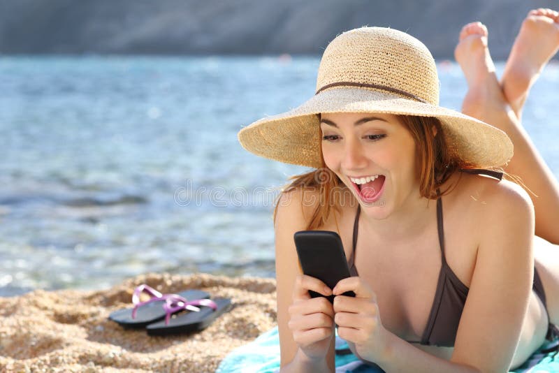Donna sorpresa divertente che guarda media sociali in uno Smart Phone sulla spiaggia