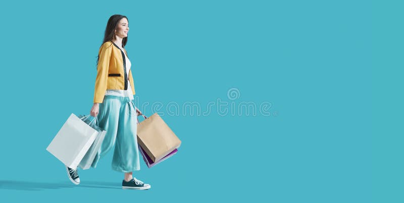 Donna sorridente che cammina e tiene le borse della spesa fotografia stock libera da diritti Donna sorridente che cammina e tiene le borse della spesa fotografia stock libera da diritti