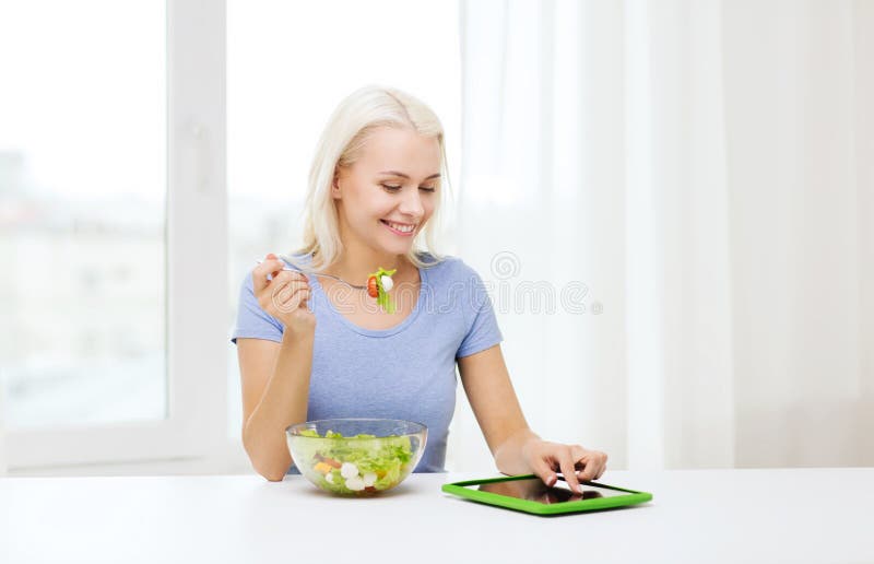 Healthy eating, dieting and people concept - smiling young woman with tablet pc computer eating vegetable salad at home. Healthy eating, dieting and people concept - smiling young woman with tablet pc computer eating vegetable salad at home