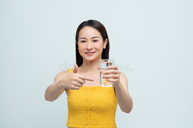 Donna sorridente che tiene in mano un bicchiere d'acqua e punta. promuove l'idratazione e uno stile di vita sano su uno sfondo lum immagini stock libere da diritti