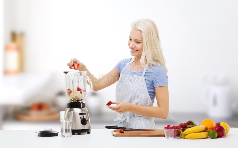 Healthy eating, cooking, vegetarian food, dieting and people concept - smiling young woman putting fruits and berries for fruit shake to blender shaker over kitchen background. Healthy eating, cooking, vegetarian food, dieting and people concept - smiling young woman putting fruits and berries for fruit shake to blender shaker over kitchen background