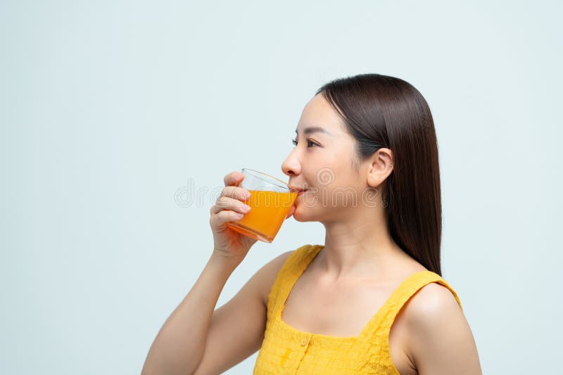 Donna sorridente con un vestito giallo che regge un bicchiere di succo d'arancia fresco in un ambiente luminoso fotografie stock