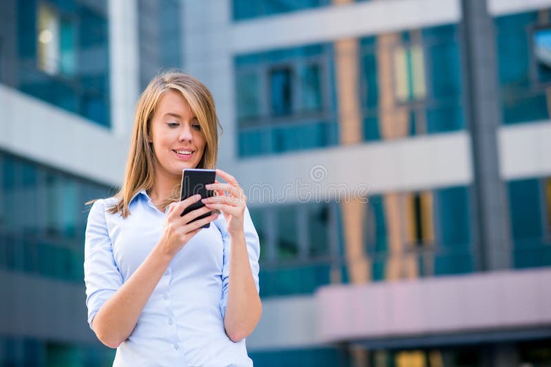Donna sorridente di affari che ascolta la chiamata sullo smartphone davanti al suo ufficio fotografia stock Donna sorridente di affari che ascolta la chiamata sullo smartphone davanti al suo ufficio fotografia stock