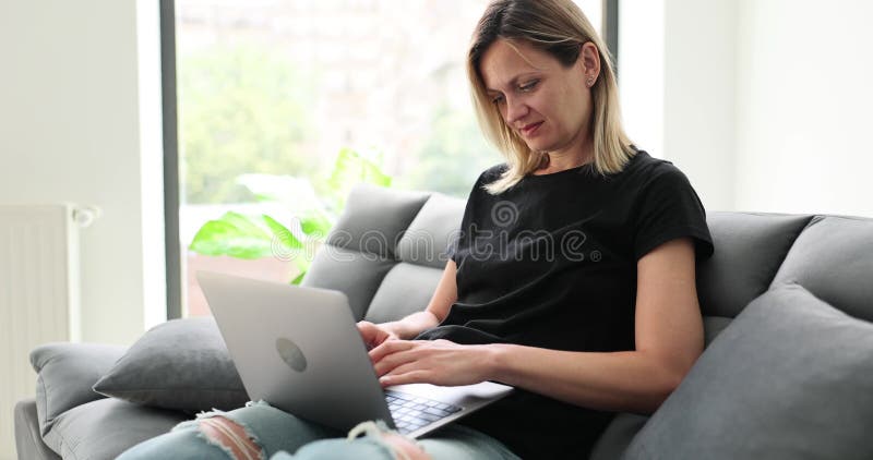 Donna sorridente seduta sul divano, con un portatile e guardando il messaggio sullo schermo