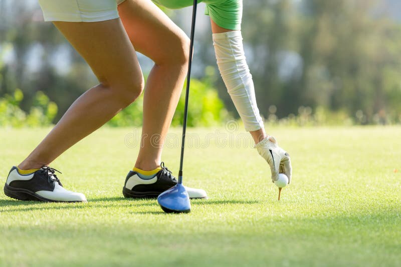 Donna sportiva asiatica della mano che mette palla da golf sul T con il club nel campo da golf sulla sera in tempo per lo sport s fotografia stock libera da diritti Donna sportiva asiatica della mano che mette palla da golf sul T con il club nel campo da golf sulla sera in tempo per lo sport s fotografia stock libera da diritti