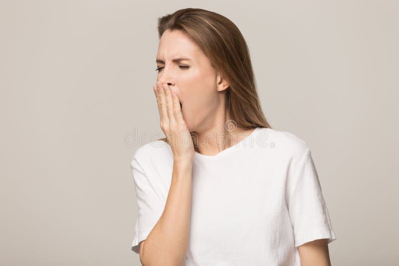 Sleepy tired young woman with closed eyes yawning, covering mouth with hand, attractive female in white t-shirt feeling lack of sleep and energy, boredom, fatigue isolated on studio background. Sleepy tired young woman with closed eyes yawning, covering mouth with hand, attractive female in white t-shirt feeling lack of sleep and energy, boredom, fatigue isolated on studio background