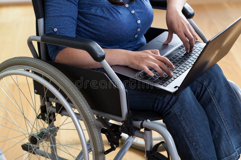 Donna su una sedia a rotelle con il computer portatile fotografia stock Donna su una sedia a rotelle con il computer portatile fotografia stock