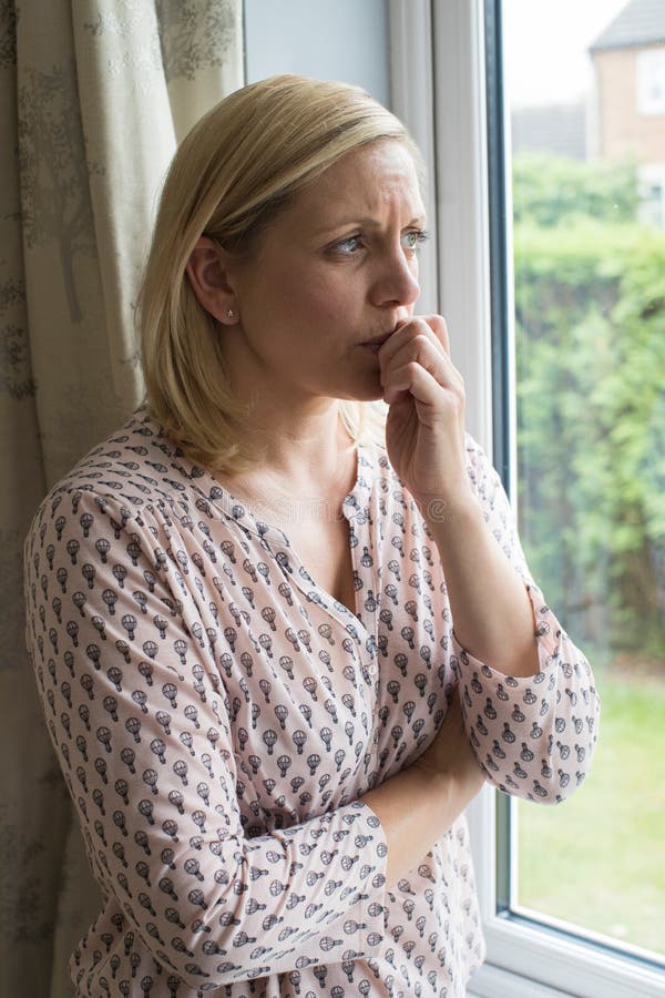 Donna triste che soffre dall'agorafobia che guarda dalla finestra immagine stock Donna triste che soffre dall'agorafobia che guarda dalla finestra immagine stock