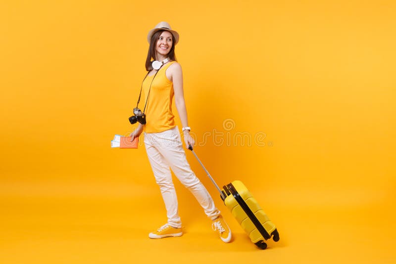 Donna turistica in abbigliamento casual di estate, cappello del viaggiatore con le cuffie sul collo isolato su fondo giallo aranc