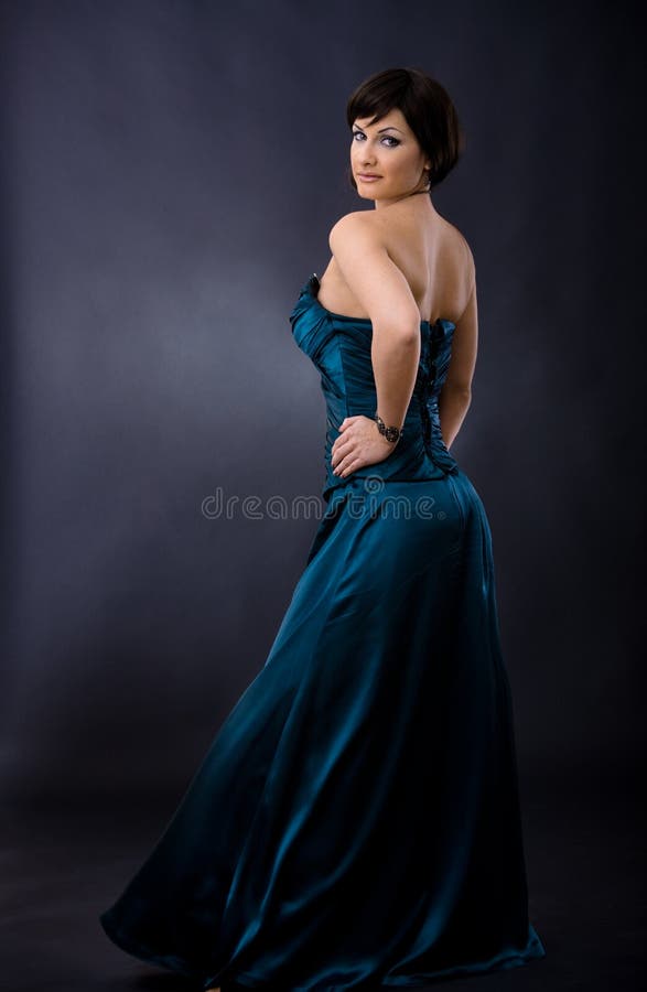 Studio portrait of beautiful young woman wearing dark blue evening dress, posing with hands on hip, smiling, looking back. Studio portrait of beautiful young woman wearing dark blue evening dress, posing with hands on hip, smiling, looking back.