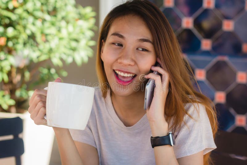 Donne asiatiche di affari di sorriso felice che utilizzano telefono cellulare di conversazione che si siede nel caffè e che tiene fotografia stock Donne asiatiche di affari di sorriso felice che utilizzano telefono cellulare di conversazione che si siede nel caffè e che tiene fotografia stock