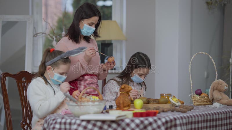 Donne caucasiche concentrate in coronavirus mascherine che colorano uova al chiuso di Pasqua. madre concentrata e video d archivio