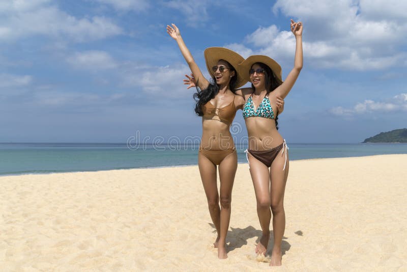 Donne sexy asiatiche in bikini, nel cappello di paglia d'uso sorridente e nei sunglass, camminanti alla spiaggia, viaggio delle v fotografia stock libera da diritti Donne sexy asiatiche in bikini, nel cappello di paglia d'uso sorridente e nei sunglass, camminanti alla spiaggia, viaggio delle v fotografia stock libera da diritti