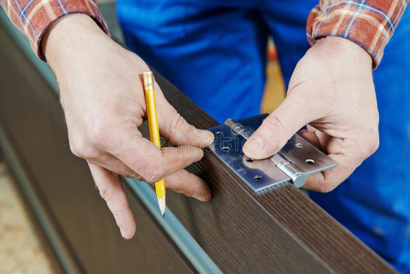 Close-up carpenter process of wood door hinge installation.