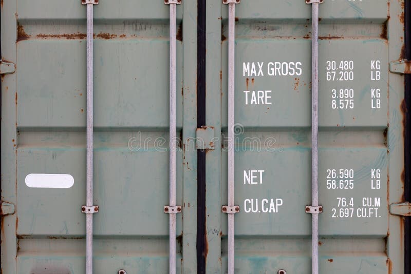 The doors of a large old container are painted in close-up in green with rust, with pipe-type locks and white lettering indicating stock photo The doors of a large old container are painted in close-up in green with rust, with pipe-type locks and white lettering indicating stock photo