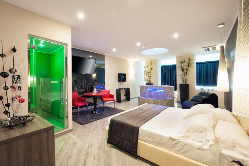 Double en-suite motel bedroom with shower, comfortable double bed and seating area in neutral decor illuminated at night. Double en-suite motel bedroom with shower, comfortable double bed and seating area in neutral decor illuminated at night