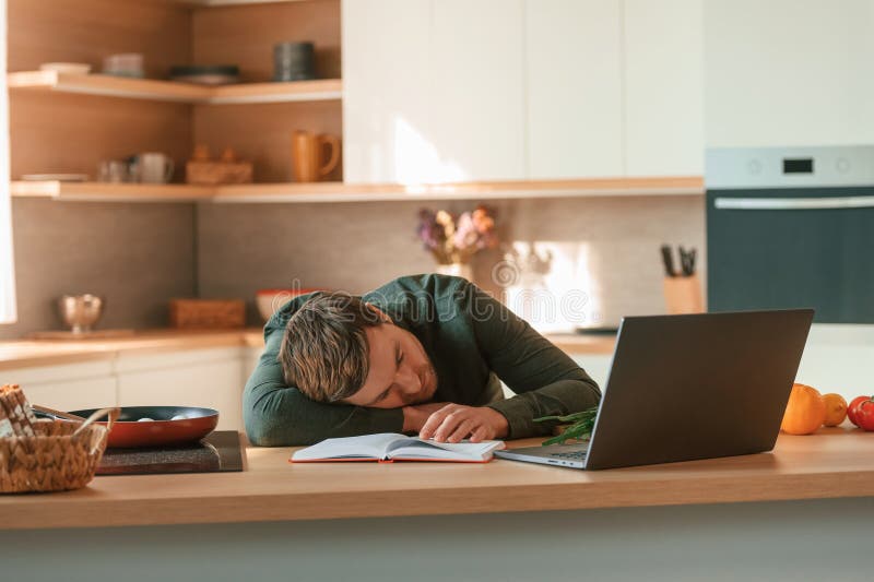 Dormire al tavolo con il portatile stanco. il bel ragazzo è in cucina di giorno fotografia stock