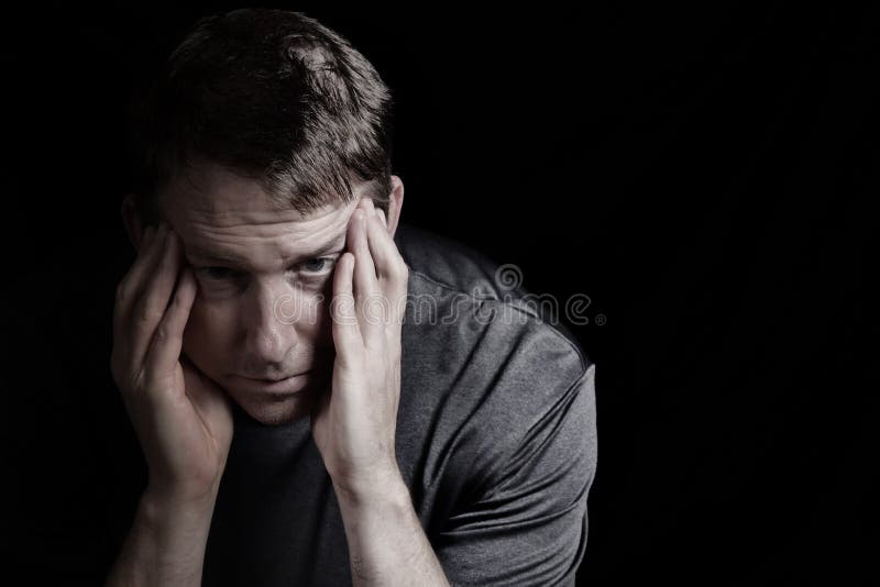 Closeup front view of mature man with head down, touching his temples, while displaying depression on black background. Closeup front view of mature man with head down, touching his temples, while displaying depression on black background