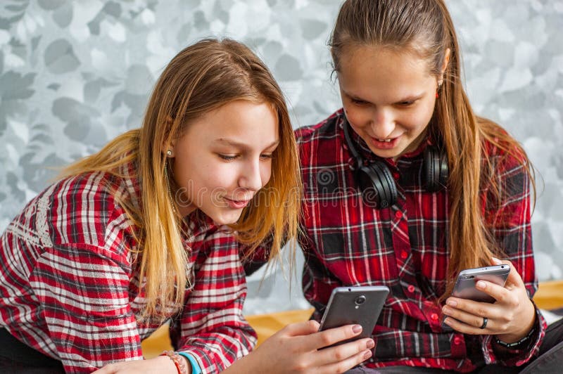 Dos adolescentes jovenes que usan los tel?fonos m?viles mientras que se sienta en un sof? en casa foto de archivo Dos adolescentes jovenes que usan los tel?fonos m?viles mientras que se sienta en un sof? en casa foto de archivo