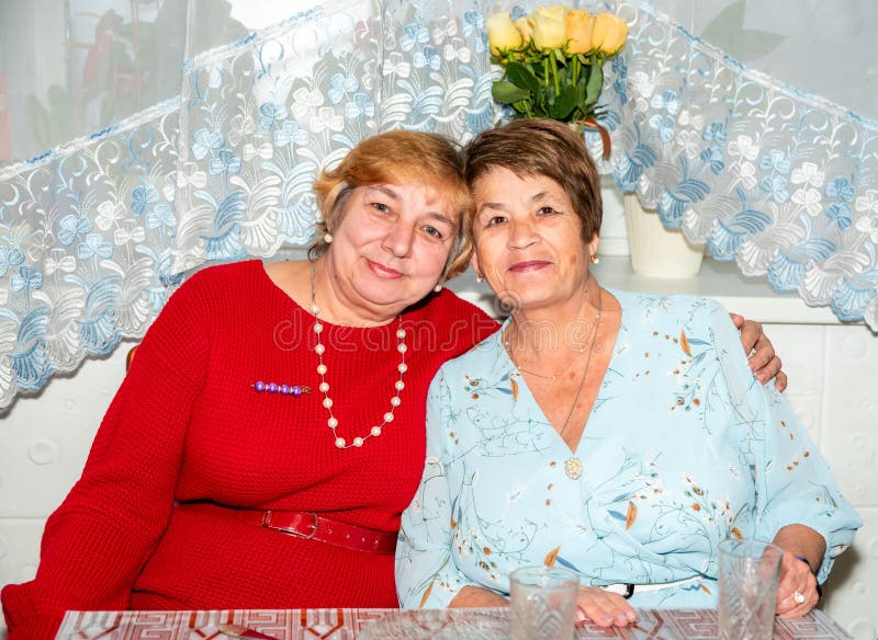 Dos alegres mujeres rusas de 60 y 71 años sonríen y abrazan en casa celebrando su amistad de toda la vida imagenes de archivo