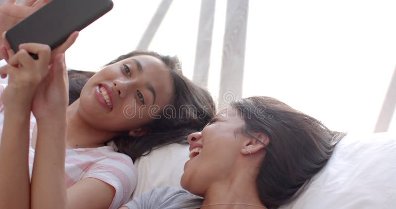Dos amigas de una adolescente birracial acostadas en casa mirando el comprimido almacen de video