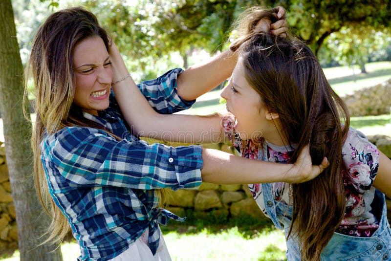 Unhappy girls fighting angry pulling long hair in park. Unhappy girls fighting angry pulling long hair in park